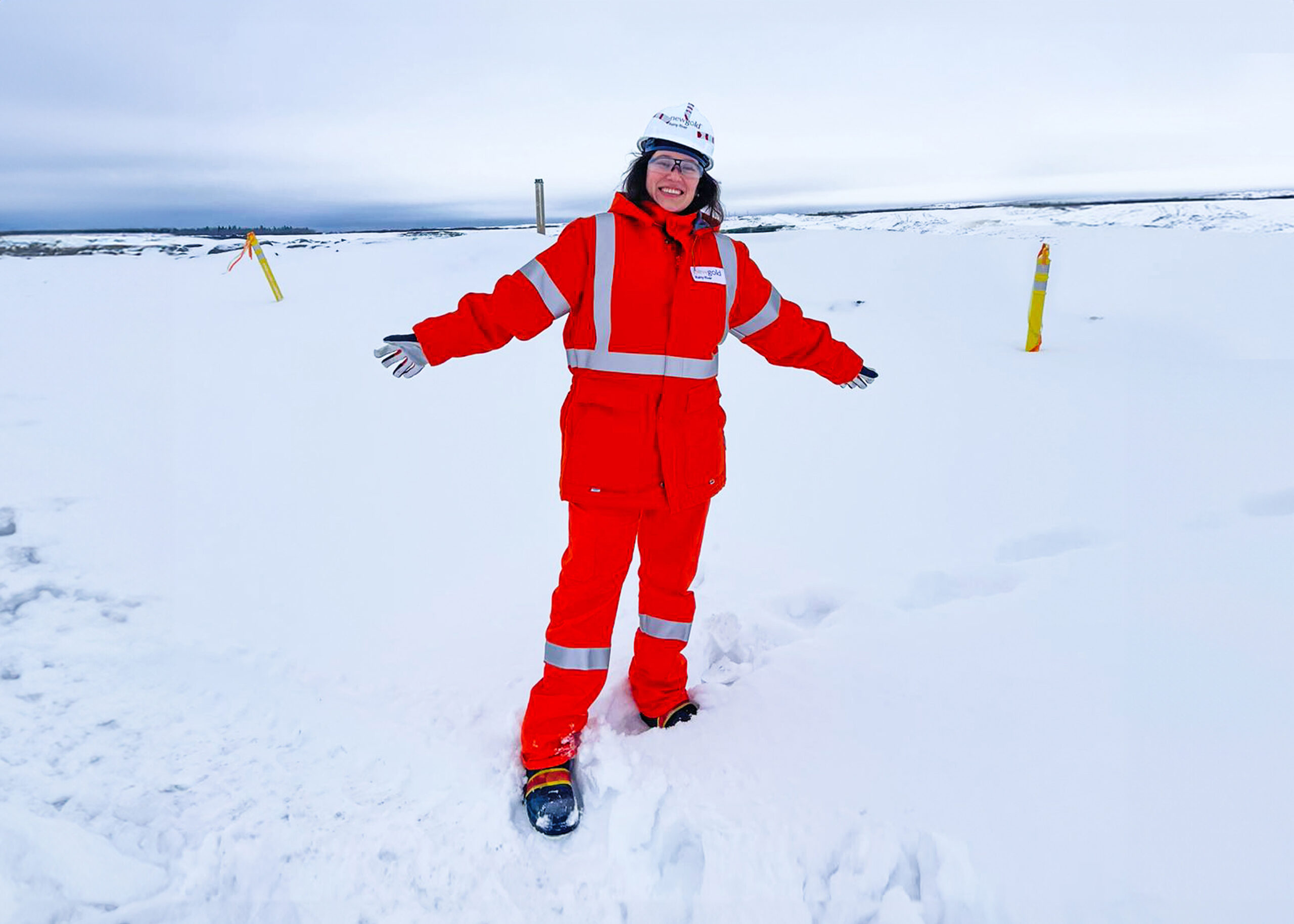 Belén stands in orange mine coveralls in front of a snowy landscape
